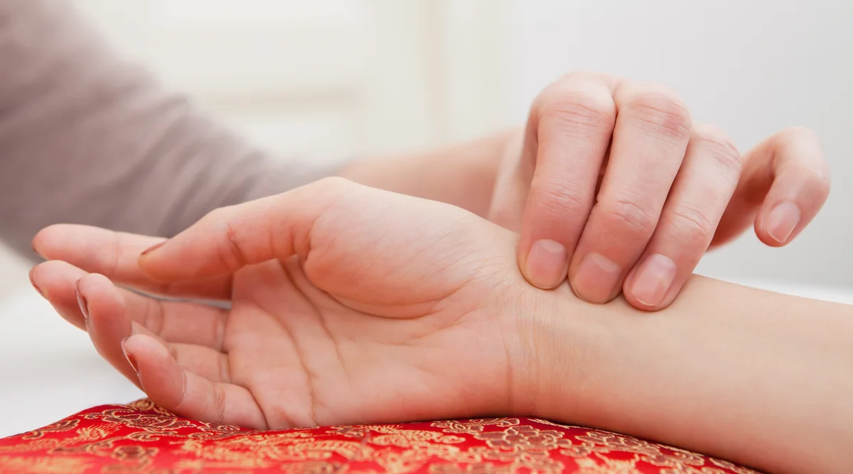 Pulsdiagnostik: Ertasten des Pulses am Handgelenk auf einem roten Seidenkissen