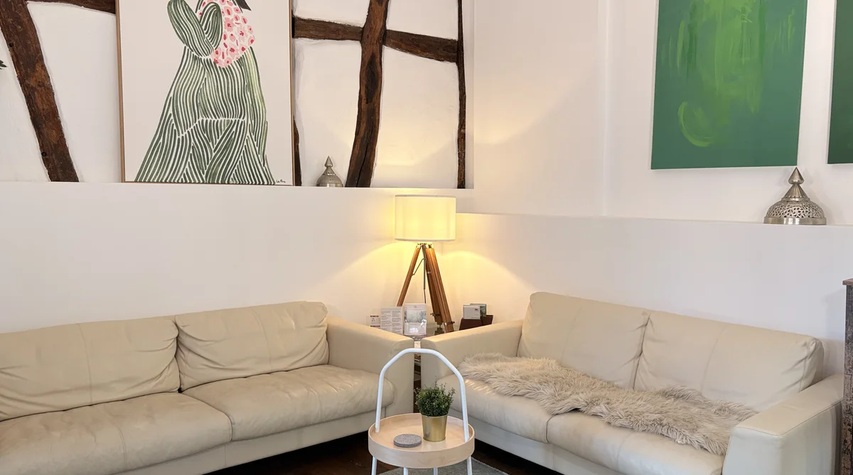 Wartebereich der Naturheilpraxis Deja-Lausmann in Eitorf mit Fachwerk, Sofas und grünen Bildern